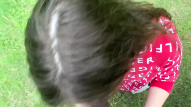 Asian woman with long dark hair in red LETTER shirt on grass park POV