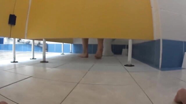 Fresh young teen bare feet under yellow stall in public shower bathroom